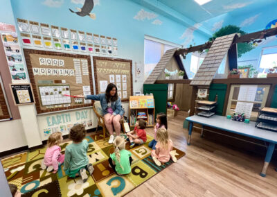 A picture of a teacher teaching 6 children sitting on the carpet below her in a thematically decorated Kids Junction classroom.