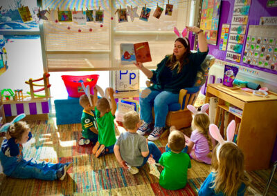 A picture of a teacher reading to 7 kids on the carpet below her in a thematically decorated Kids Junction classroom.