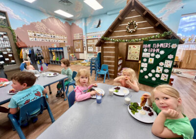 A picture of children sitting in a thematically decorated Kids Junction classroom eating a meal at their tables and looking at the camera.
