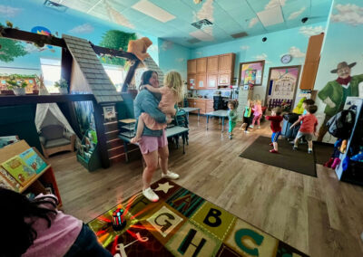 A picture of a thematically decorated Kids Junction classroom full of students. The teacher in the classroom is holding a little girl and dancing,