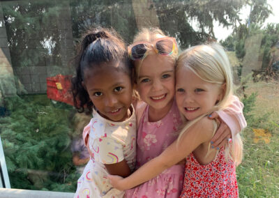 A picture of three little girls standing on a bench and hugging each other while smiling at the camera.