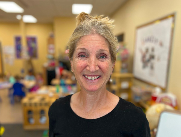 A portrait-style picture of Pam standing in a classroom and smiling at the camera.