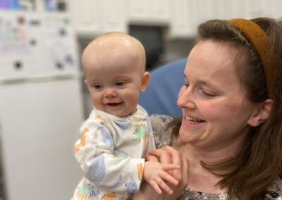 A picture of a Kids Junction teacher sitting in a rocking chair and holding a little baby and smiling at him as he's smiling at something in the distance.