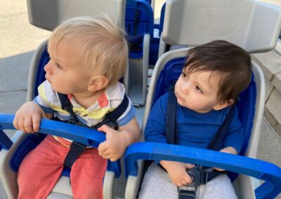 A picture of two babies from the Infants and Toddlers program in a group stroller looking to the left.
