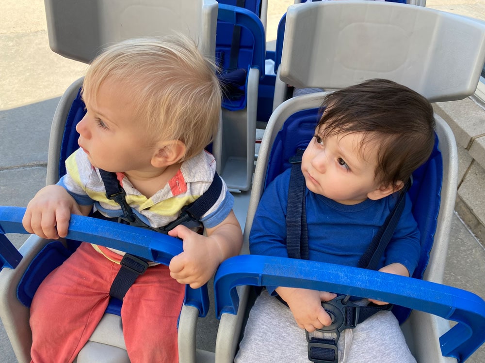 A picture of two babies from the Infants and Toddlers program in a group stroller looking to the left.