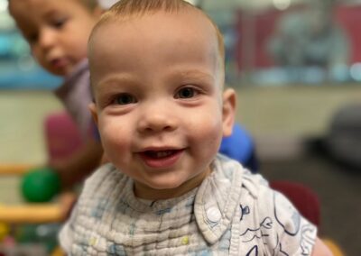 A close-up picture of a baby smiling at the camera in the Infants and Toddlers class.