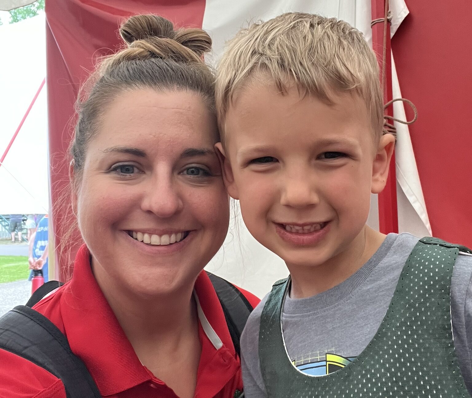 A picture of a member of the administrative staff standing next to a young child and smiling at the camera.