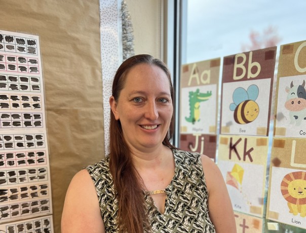 A portrait-style picture of Pam standing in a classroom and smiling at the camera.